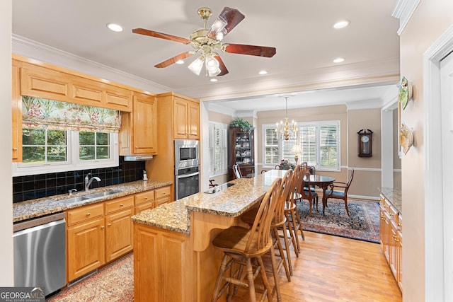 kitchen with tasteful backsplash, ceiling fan with notable chandelier, a kitchen island, stainless steel appliances, and light hardwood / wood-style flooring