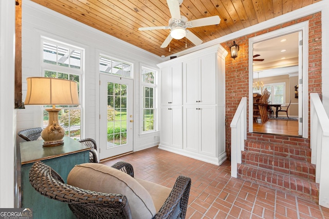 interior space featuring ceiling fan with notable chandelier, a wealth of natural light, brick wall, and wood ceiling