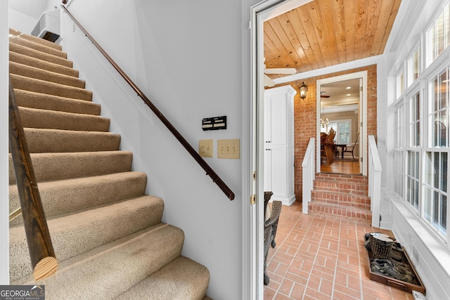 stairs with brick wall, crown molding, and wooden ceiling