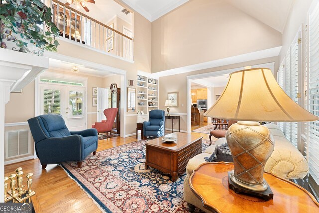 living room with light wood-type flooring, crown molding, french doors, and high vaulted ceiling