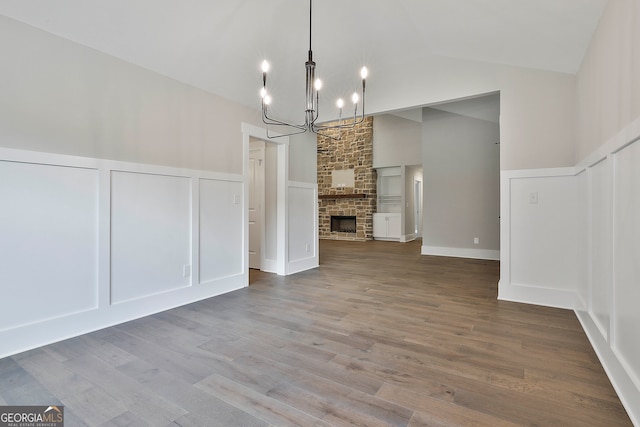 unfurnished dining area with a chandelier, lofted ceiling, wood-type flooring, and a fireplace