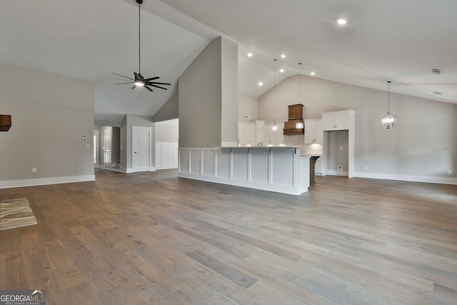 unfurnished living room featuring ceiling fan with notable chandelier, light hardwood / wood-style flooring, and high vaulted ceiling