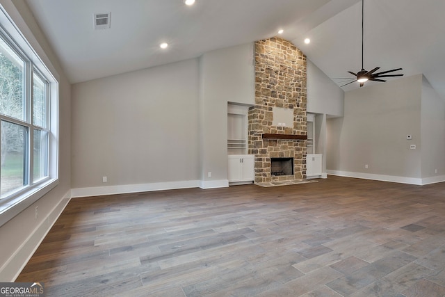 unfurnished living room with a stone fireplace, a wealth of natural light, hardwood / wood-style flooring, and ceiling fan