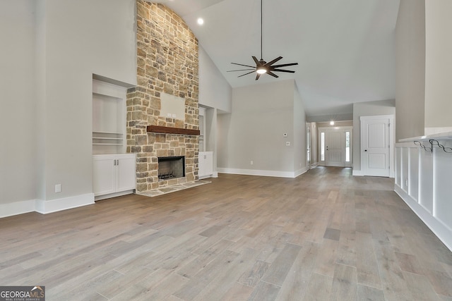 unfurnished living room featuring light hardwood / wood-style floors, high vaulted ceiling, ceiling fan, a fireplace, and built in features