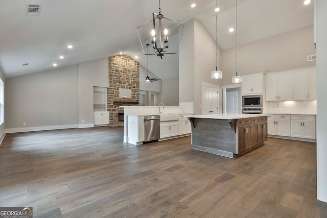 kitchen with white cabinets, high vaulted ceiling, dark hardwood / wood-style floors, appliances with stainless steel finishes, and a large island with sink