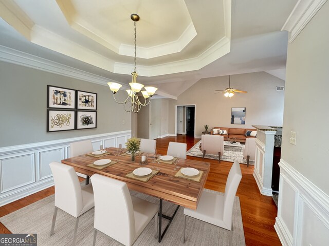 dining area with light wood-type flooring, a tray ceiling, ceiling fan with notable chandelier, lofted ceiling, and ornamental molding