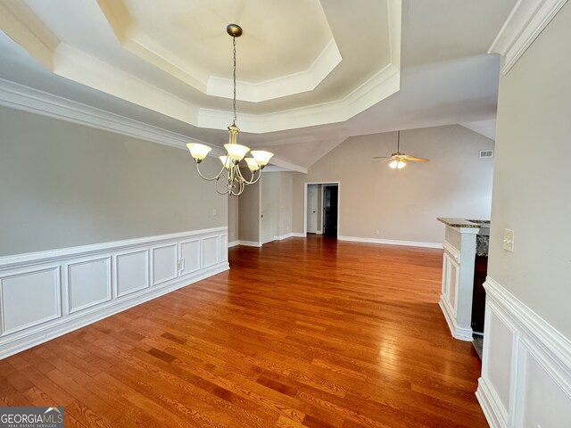 unfurnished dining area featuring ceiling fan with notable chandelier, a tray ceiling, ornamental molding, and wood-type flooring