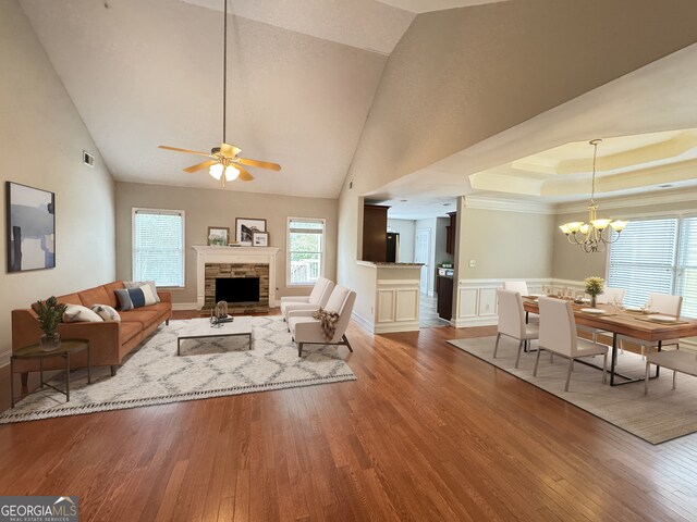 living room featuring light hardwood / wood-style floors, ceiling fan with notable chandelier, a fireplace, and high vaulted ceiling