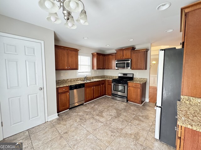 kitchen with sink, an inviting chandelier, stainless steel appliances, light tile patterned floors, and light stone countertops