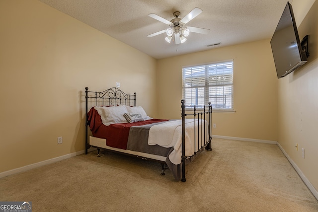 bedroom with ceiling fan, light colored carpet, and a textured ceiling