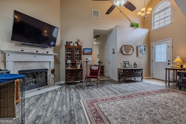 living room featuring wood-type flooring, a tiled fireplace, a towering ceiling, and ceiling fan