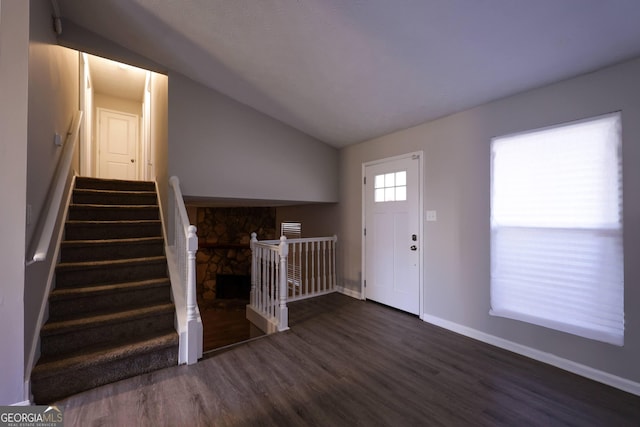 foyer entrance featuring a stone fireplace, dark hardwood / wood-style floors, and vaulted ceiling