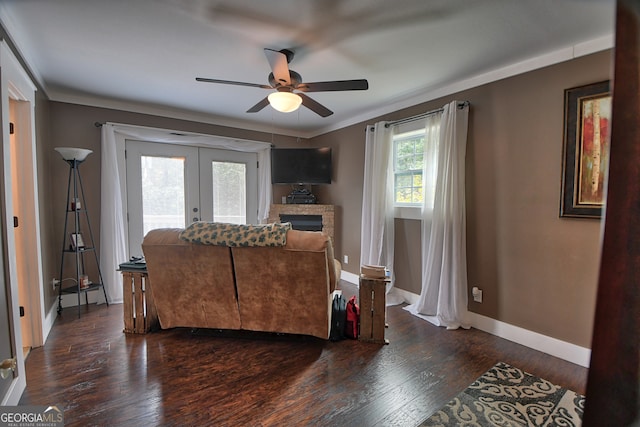 living room with dark wood-type flooring, a fireplace, crown molding, ceiling fan, and french doors