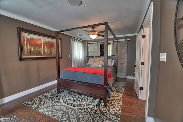 bedroom with ornamental molding, ceiling fan, dark wood-type flooring, and a barn door