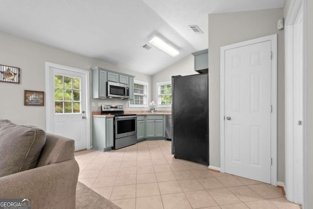 kitchen with a wealth of natural light, vaulted ceiling, appliances with stainless steel finishes, and light tile patterned floors