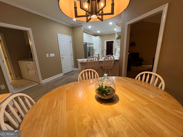 dining room featuring sink, a notable chandelier, independent washer and dryer, hardwood / wood-style floors, and crown molding