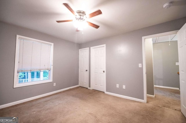 unfurnished bedroom featuring ceiling fan, light colored carpet, and two closets