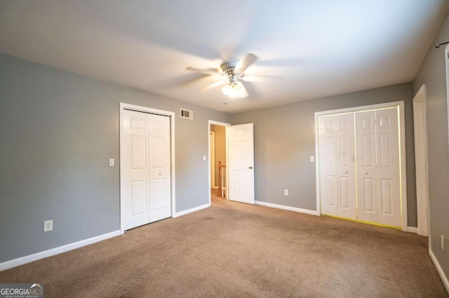 unfurnished bedroom featuring carpet floors, ceiling fan, and multiple closets