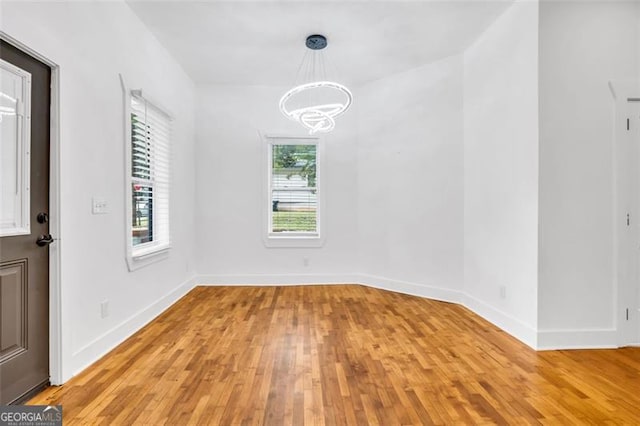 spare room featuring an inviting chandelier and light hardwood / wood-style flooring