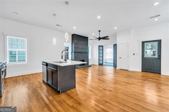 kitchen featuring sink, an island with sink, light hardwood / wood-style flooring, decorative light fixtures, and a large fireplace