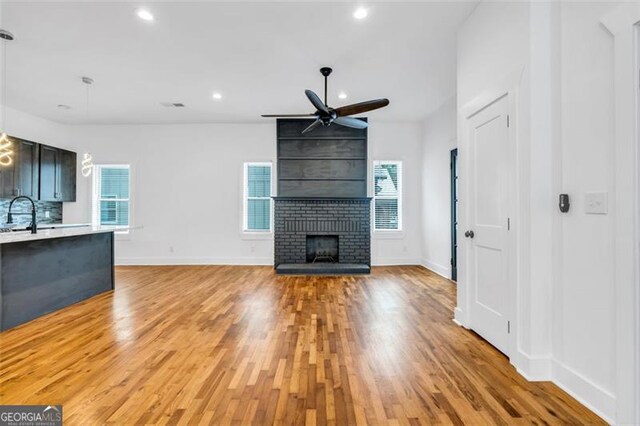 unfurnished living room featuring light hardwood / wood-style flooring, ceiling fan, a brick fireplace, and a wealth of natural light