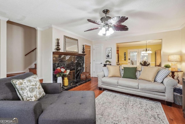 living room featuring ceiling fan with notable chandelier, hardwood / wood-style floors, a tiled fireplace, and ornamental molding