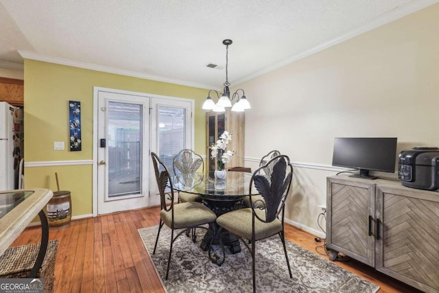 dining room featuring a textured ceiling, ornamental molding, hardwood / wood-style floors, and a chandelier