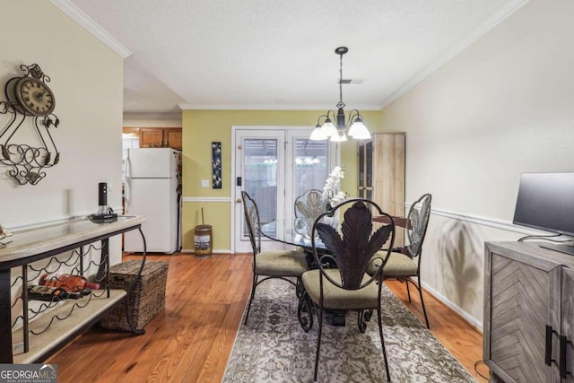 dining space with a notable chandelier, light wood-type flooring, plenty of natural light, and crown molding