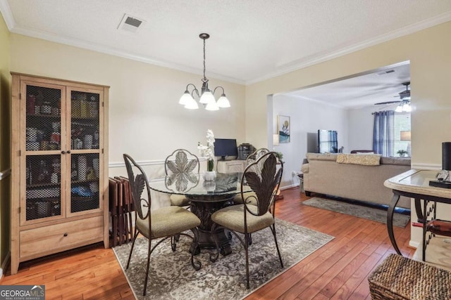 dining area with a textured ceiling, ceiling fan with notable chandelier, crown molding, and hardwood / wood-style floors