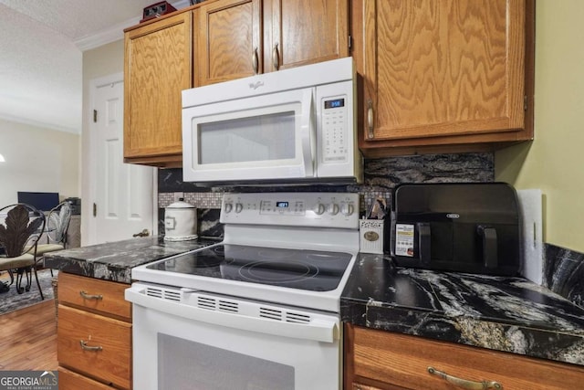 kitchen with ornamental molding, white appliances, hardwood / wood-style flooring, dark stone countertops, and decorative backsplash