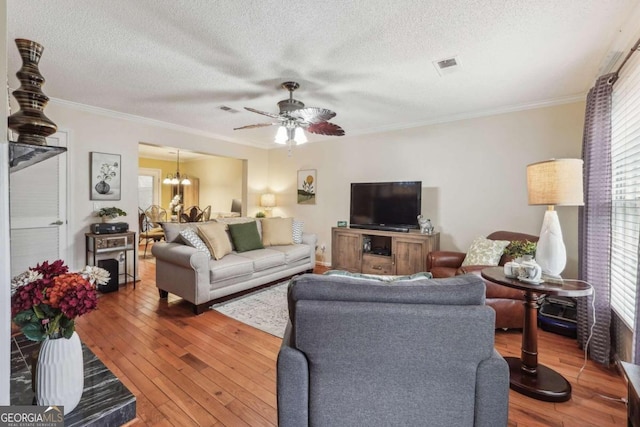 living room with wood-type flooring, a textured ceiling, ceiling fan with notable chandelier, and crown molding