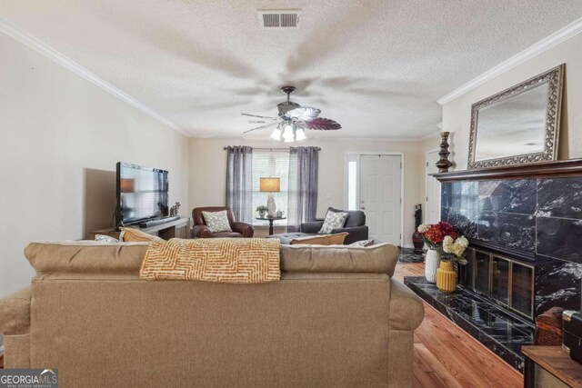 living room with a high end fireplace, a textured ceiling, hardwood / wood-style floors, ornamental molding, and ceiling fan