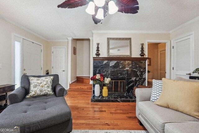 living room featuring ceiling fan, wood-type flooring, a textured ceiling, a fireplace, and crown molding