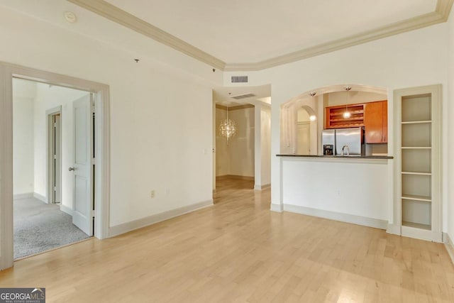 unfurnished living room with ornamental molding, an inviting chandelier, and light wood-type flooring