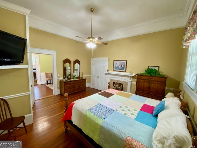 bedroom featuring ceiling fan, a tile fireplace, crown molding, and dark hardwood / wood-style flooring