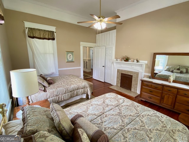 interior space with a tiled fireplace, ceiling fan, dark hardwood / wood-style floors, and crown molding