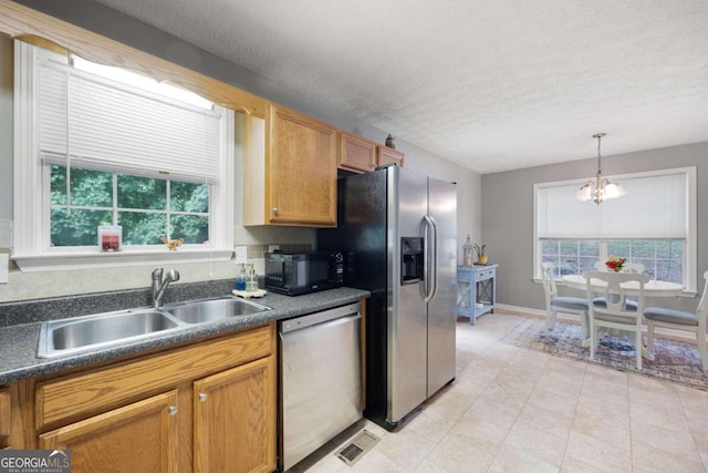 kitchen with sink, appliances with stainless steel finishes, a textured ceiling, an inviting chandelier, and pendant lighting