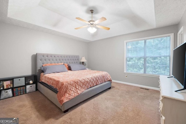 bedroom featuring a tray ceiling, a textured ceiling, light colored carpet, and ceiling fan