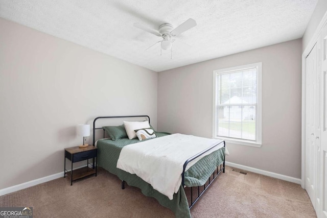 bedroom featuring a closet, a textured ceiling, light carpet, and ceiling fan