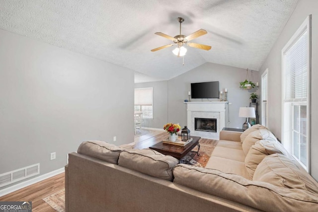 living room featuring a textured ceiling, light hardwood / wood-style floors, lofted ceiling, and ceiling fan