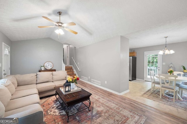 living room featuring light wood-type flooring, ceiling fan with notable chandelier, a textured ceiling, and vaulted ceiling