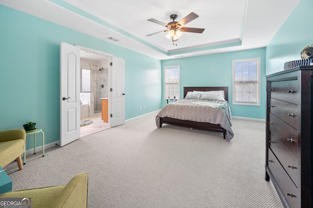 bedroom with a raised ceiling, light carpet, ensuite bathroom, and ceiling fan