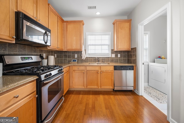 kitchen with sink, stainless steel appliances, light hardwood / wood-style floors, and washer / clothes dryer