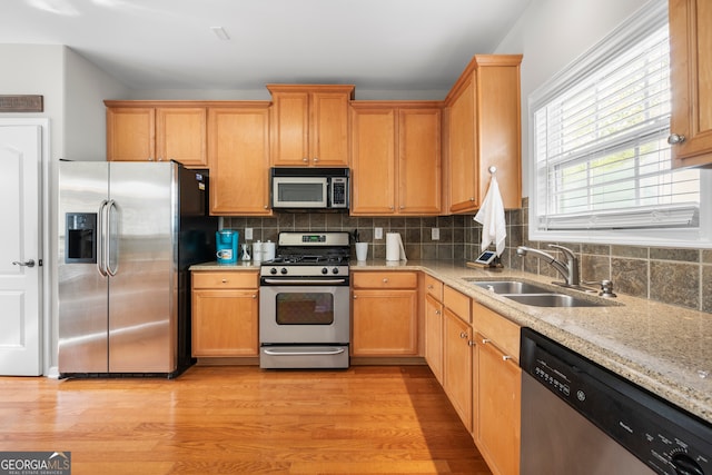 kitchen featuring decorative backsplash, light hardwood / wood-style flooring, sink, appliances with stainless steel finishes, and light stone counters