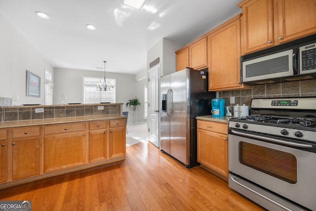 kitchen featuring appliances with stainless steel finishes, hanging light fixtures, light hardwood / wood-style floors, decorative backsplash, and a chandelier