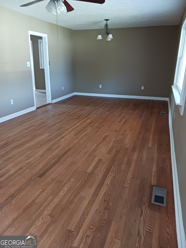 spare room with ceiling fan with notable chandelier and dark wood-type flooring