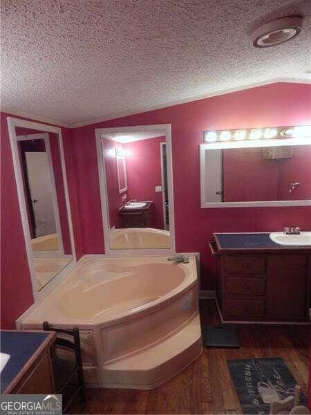 bathroom with a textured ceiling, vaulted ceiling, vanity, and hardwood / wood-style flooring