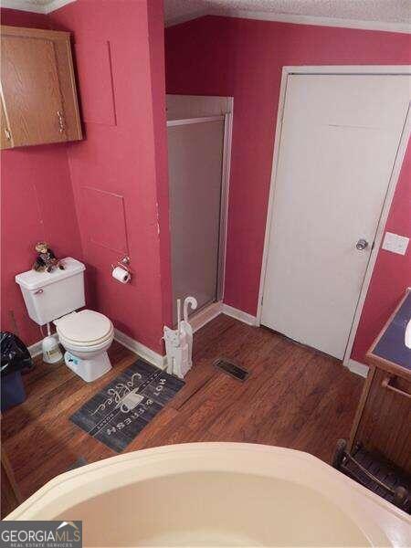 bathroom with a textured ceiling, toilet, plus walk in shower, and hardwood / wood-style flooring