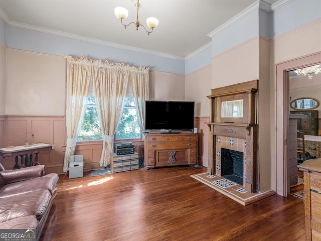 living room featuring a notable chandelier, a tiled fireplace, dark wood-type flooring, and crown molding