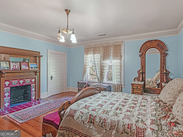 bedroom featuring ornamental molding, an inviting chandelier, a fireplace, and hardwood / wood-style floors